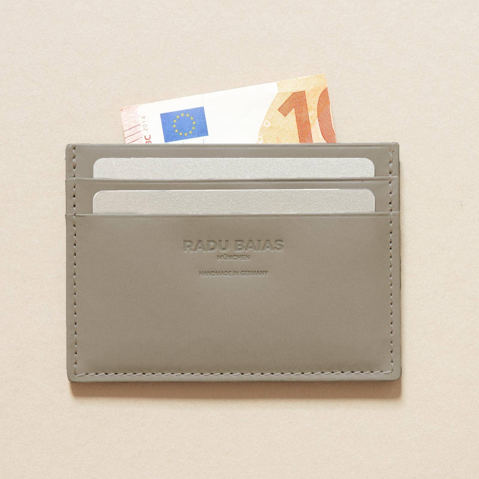 Cardholder aus Leder in Moosgrau mit Logoprägung und beispielhaft mit Karten und Geldschein befüllt