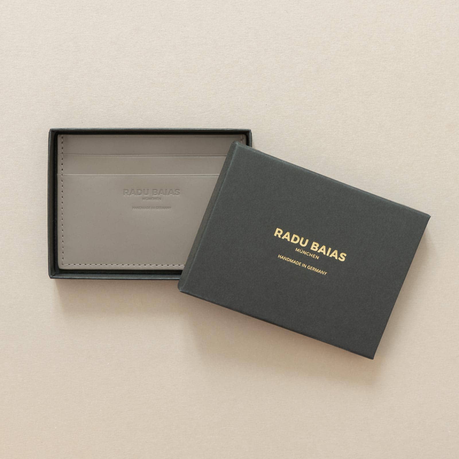 Cardholder aus Leder in Moosgrau mit Logoprägung in einer schwarzen Geschenkschachtel mit Radu Baias Logo liegend