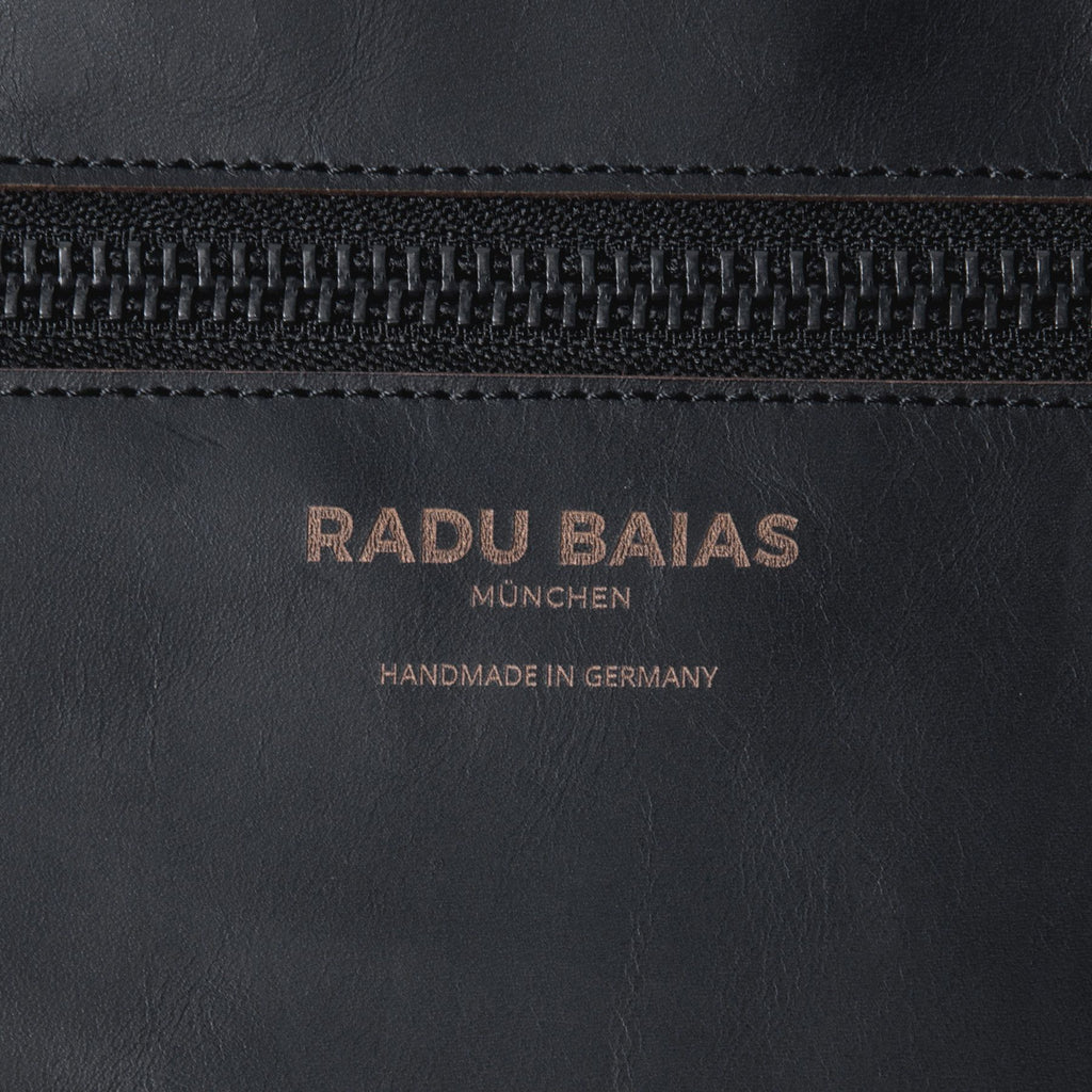 Detailansicht des gravierten Markenlogos auf einer schwarzen Crossbody Tasche aus pflanzlich gegerbtem Leder