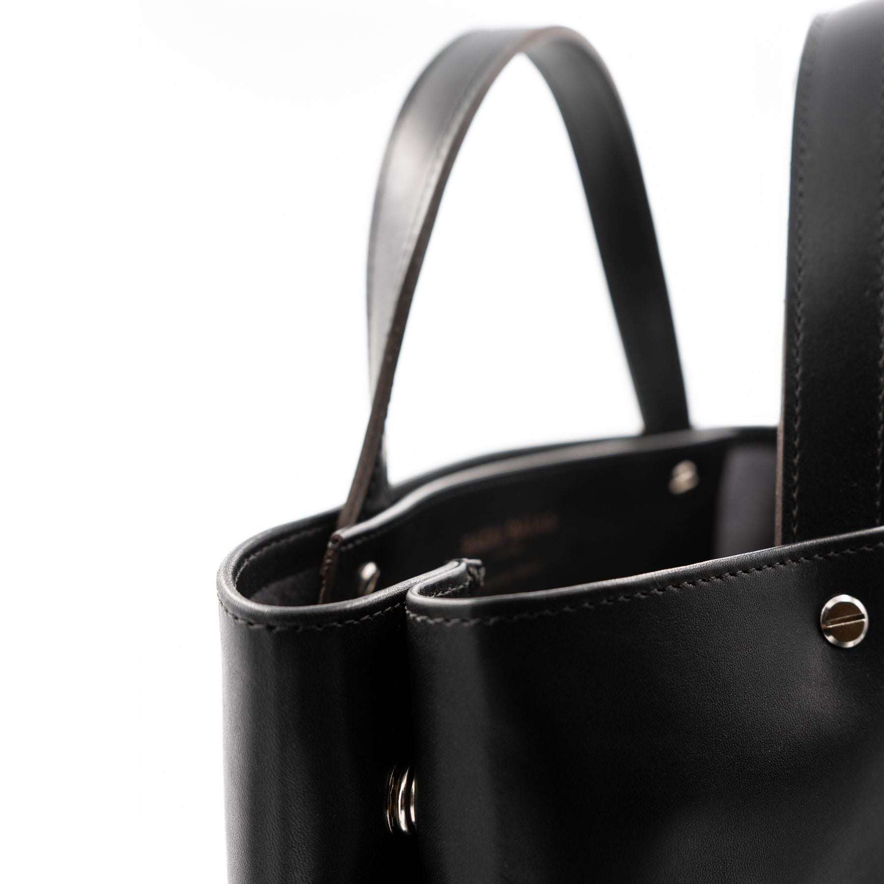 Detailansicht der seitlichen Druckknöpfe eines schwarzen Shoppers aus pflanzlich gegerbtem Sattelleder mit matter Oberfläche, kurzen Tragegriffen und silbernen Schraubnieten