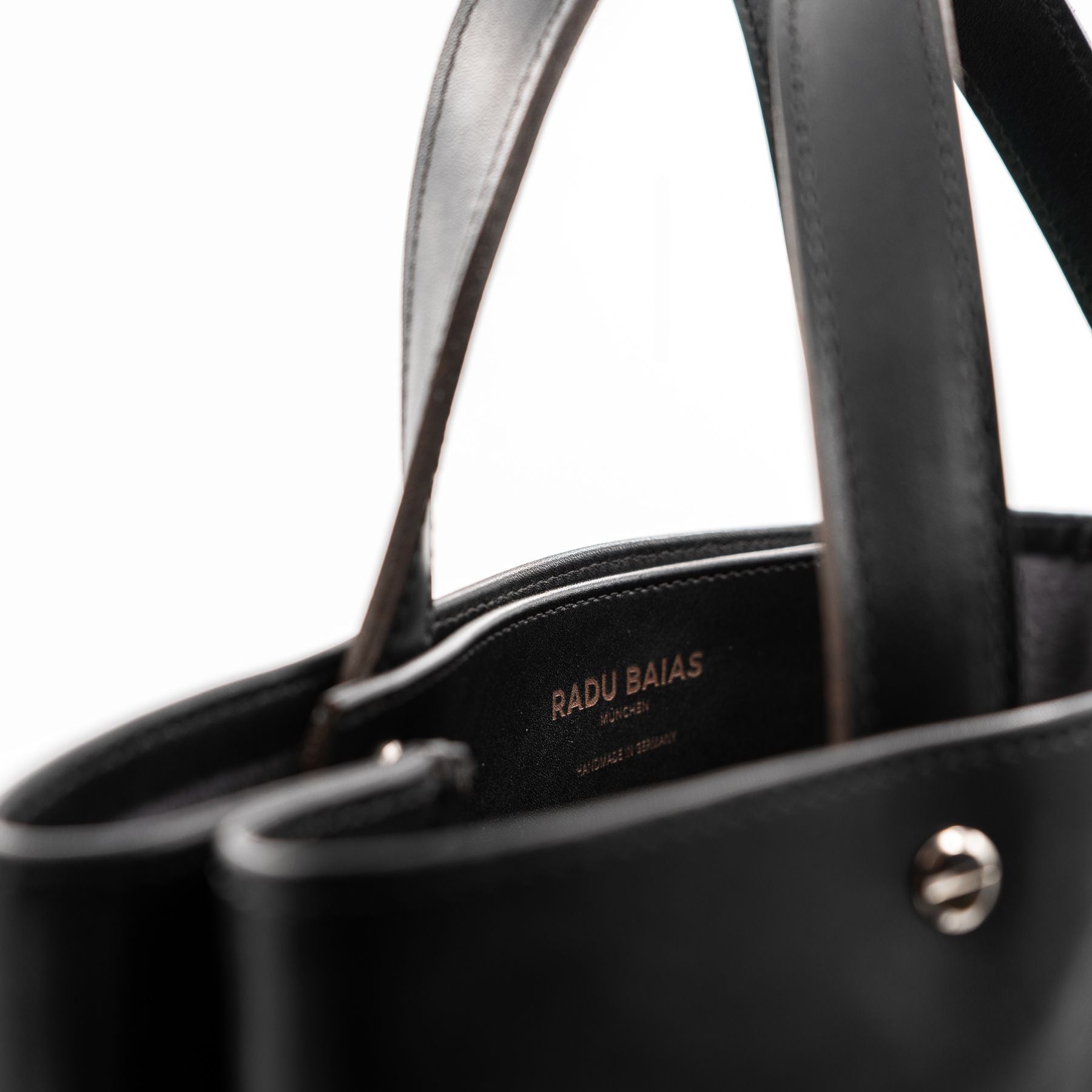 Detailansicht der Logogravur auf der Innenseite eines schwarzen Shoppers aus pflanzlich gegerbtem Sattelleder mit matter Oberfläche, kurzen Tragegriffen und silbernen Schraubnieten