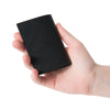 Hand hält zugeklapptes zeitloses Mini-Portemonnaie in schwarz aus pflanzlich gegerbtem Leder 