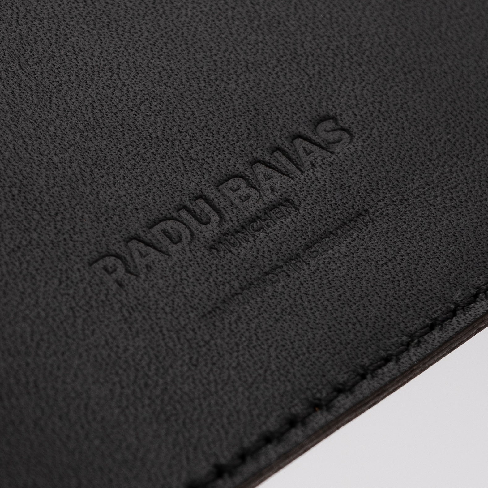 Seitliche Detailansicht der Logo-Prägung auf schwarzem Leder mit Struktur von Radu Baias München
