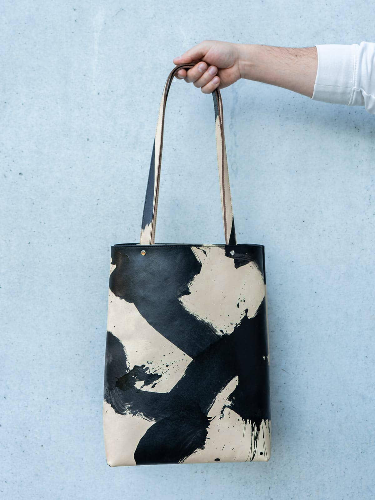 Frontale Ansicht eines abstrakt handbemalten Shoppers mit langen Henkeln in schwarz und beige von Radu Baias aus premium pflanzlich gegerbtem Olivenleder®